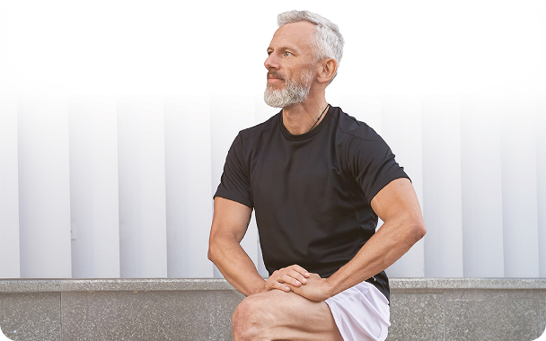 Older man sitting outdoors stretching his knee
